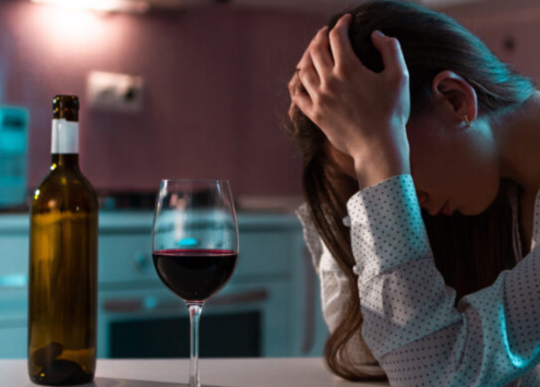 Person sat down looking distressed with hands on head, glass of wine on table.