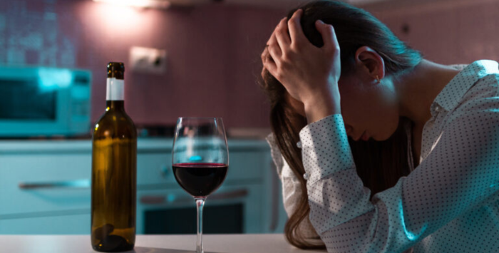 Person sat down looking distressed with hands on head, glass of wine on table.