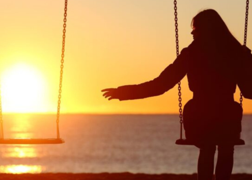 Person on a swing reaching out to the other swing which is empty