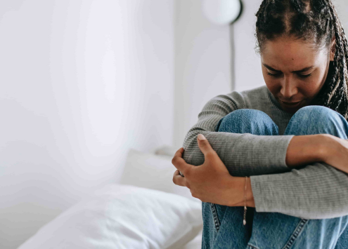 Person wrapping arms around themselves, sitting on a bed