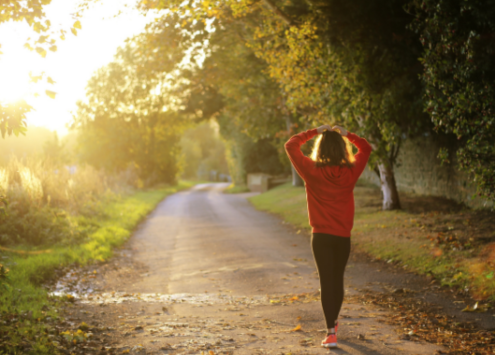 Person walking outside surrounded by trees and nature, sun shining.