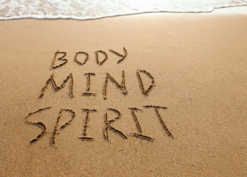 A sandy beach with 'body', 'mind' and 'spirit' written in the sand