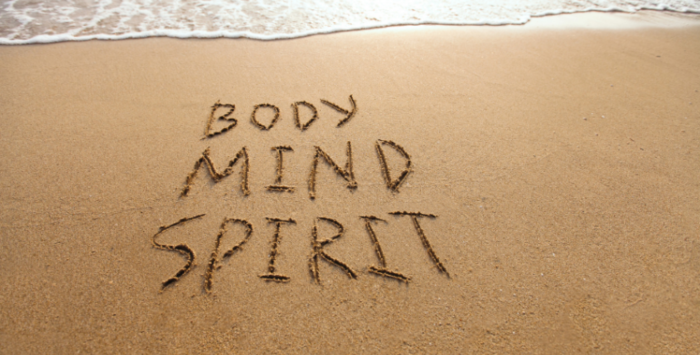 A sandy beach with 'body', 'mind' and 'spirit' written in the sand