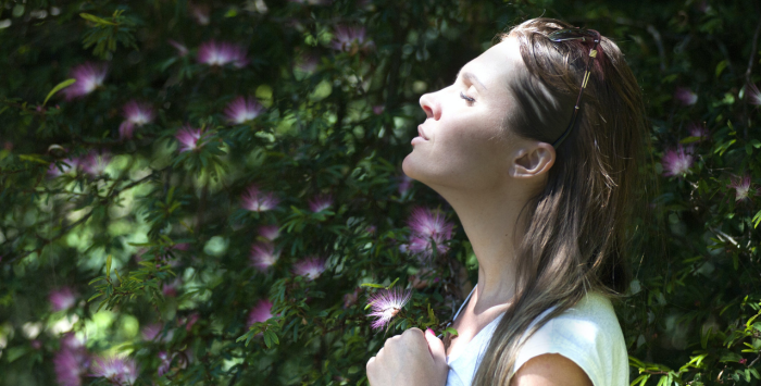 Person with eyes closed taking a deep breath in nature.